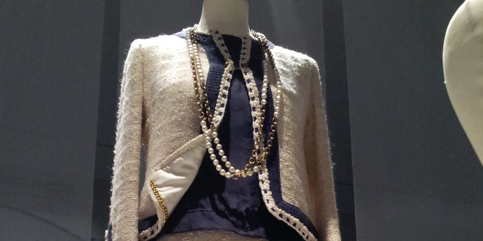 A cream wool tweed Chanel suit with a black silk blouse displayed on a mannequin