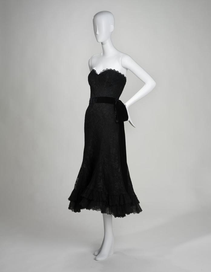 A 1958 strapless black lace evening dress by Coco Chanel with a velvet sash on a mannequin