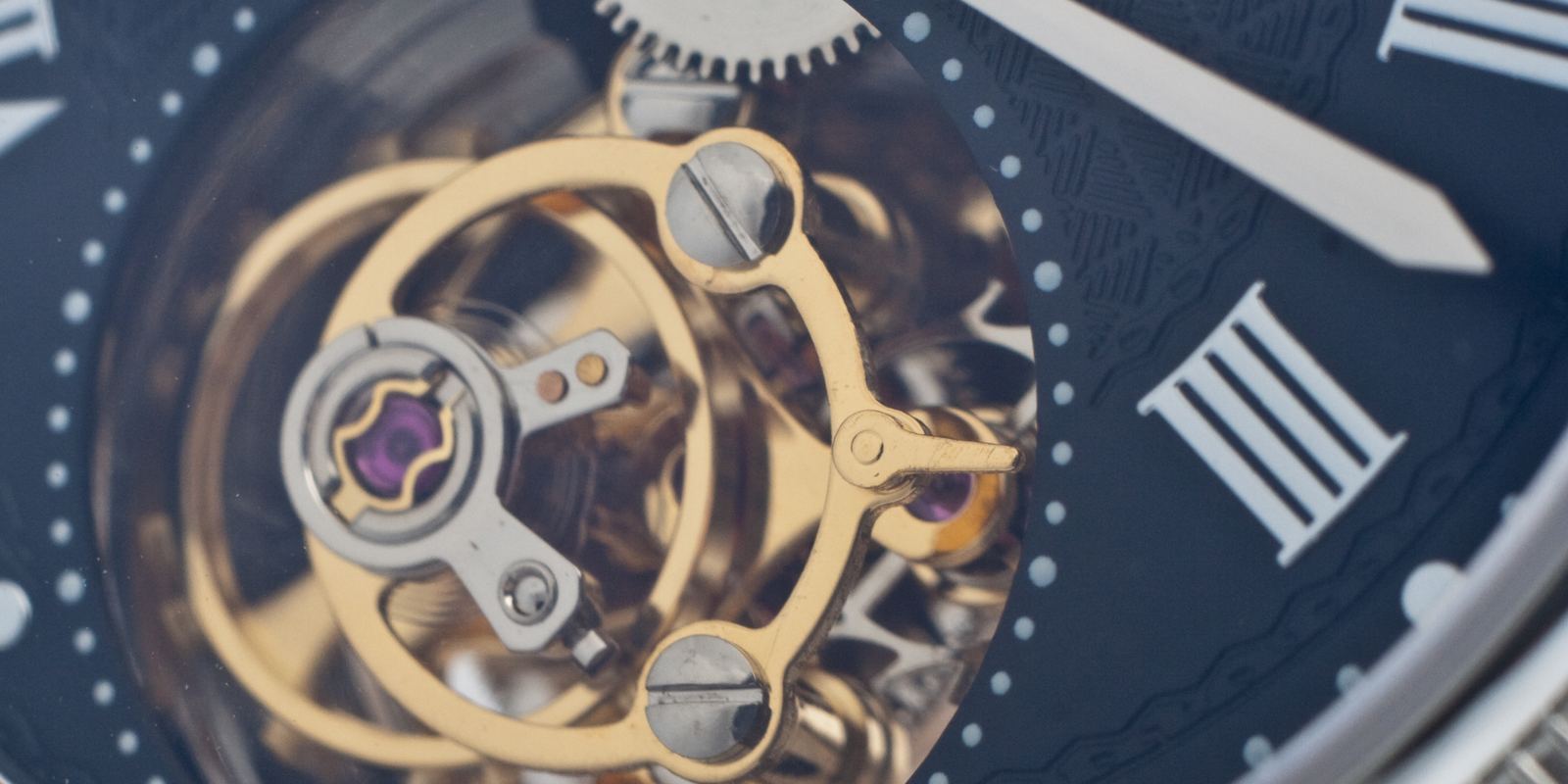 Close-up of a tourbillon cage with a gold balance wheel visible through a watch dial