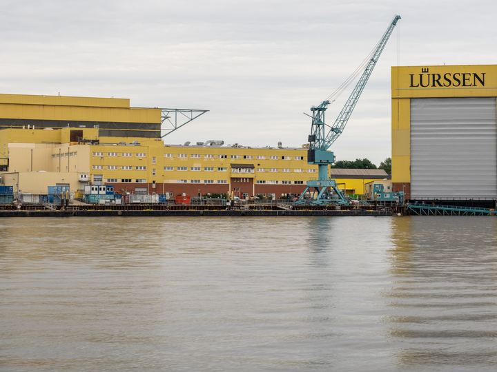 Large yellow construction halls and a crane at the Lürssen shipyard in Bremen-Vegesack beside the river