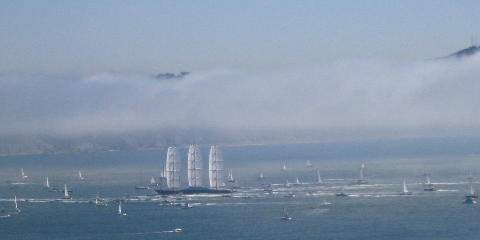 The Maltese Falcon under full sail on a bay, with fog rolling over the hills behind