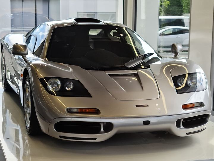A silver McLaren F1 road car shown from the front in a showroom