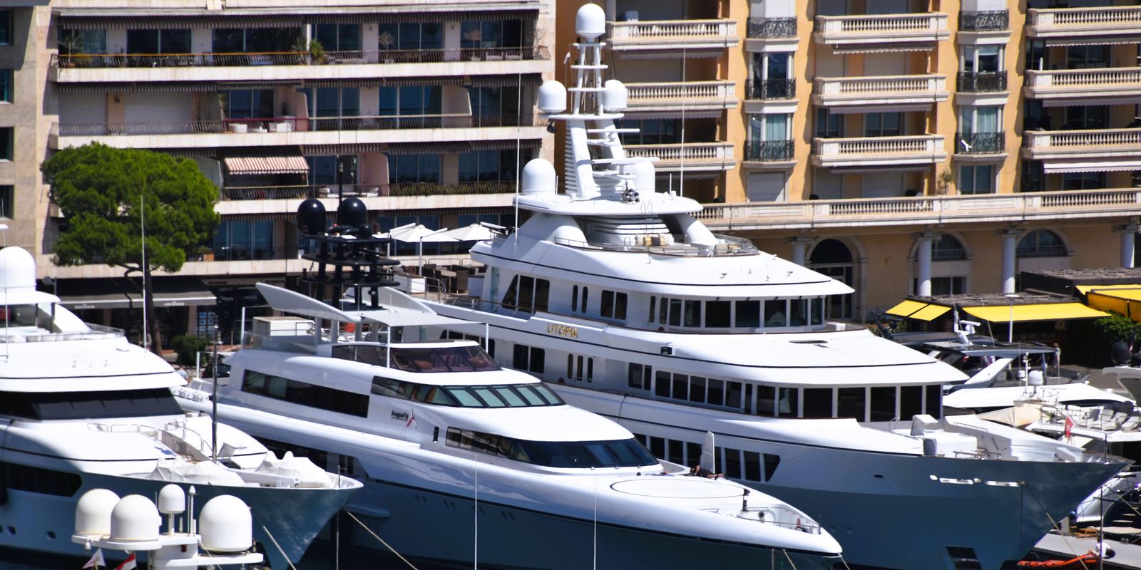 Large white motor yachts moored side by side in Port Hercules, Monaco, with apartment buildings behind