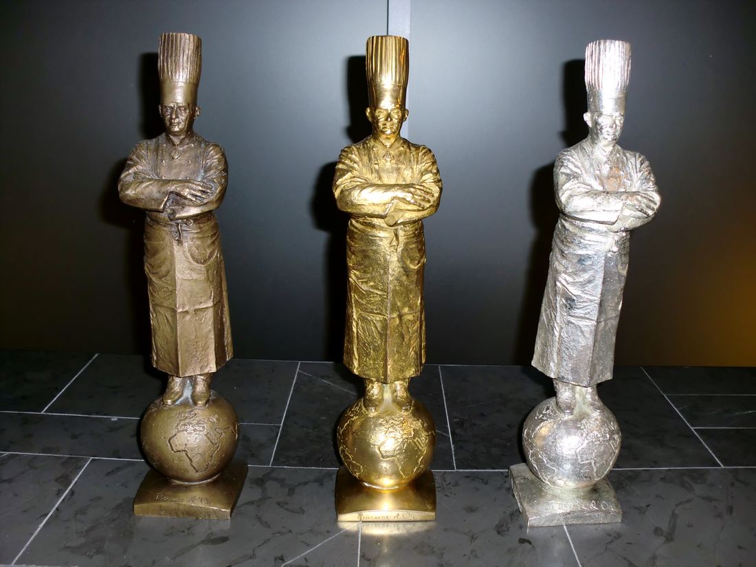Gold, silver and bronze Bocuse d'Or trophies shaped like a chef figure on a globe