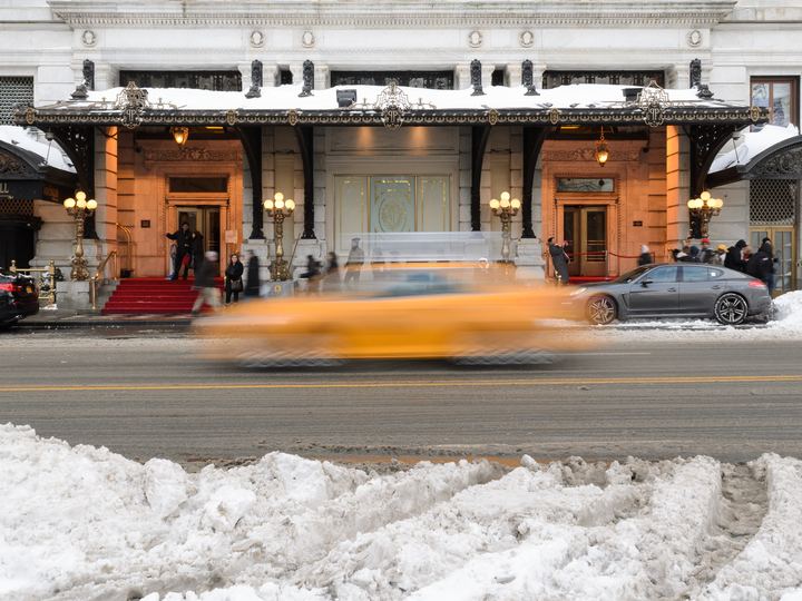 The arched entrance of The Plaza hotel in New York in winter with a yellow taxi blurring past